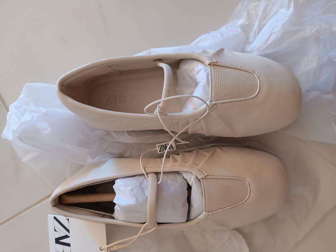 Beige, round-toe lace-up shoes, stuffed with white paper. Visible label with the text "ZARA". White paper background.