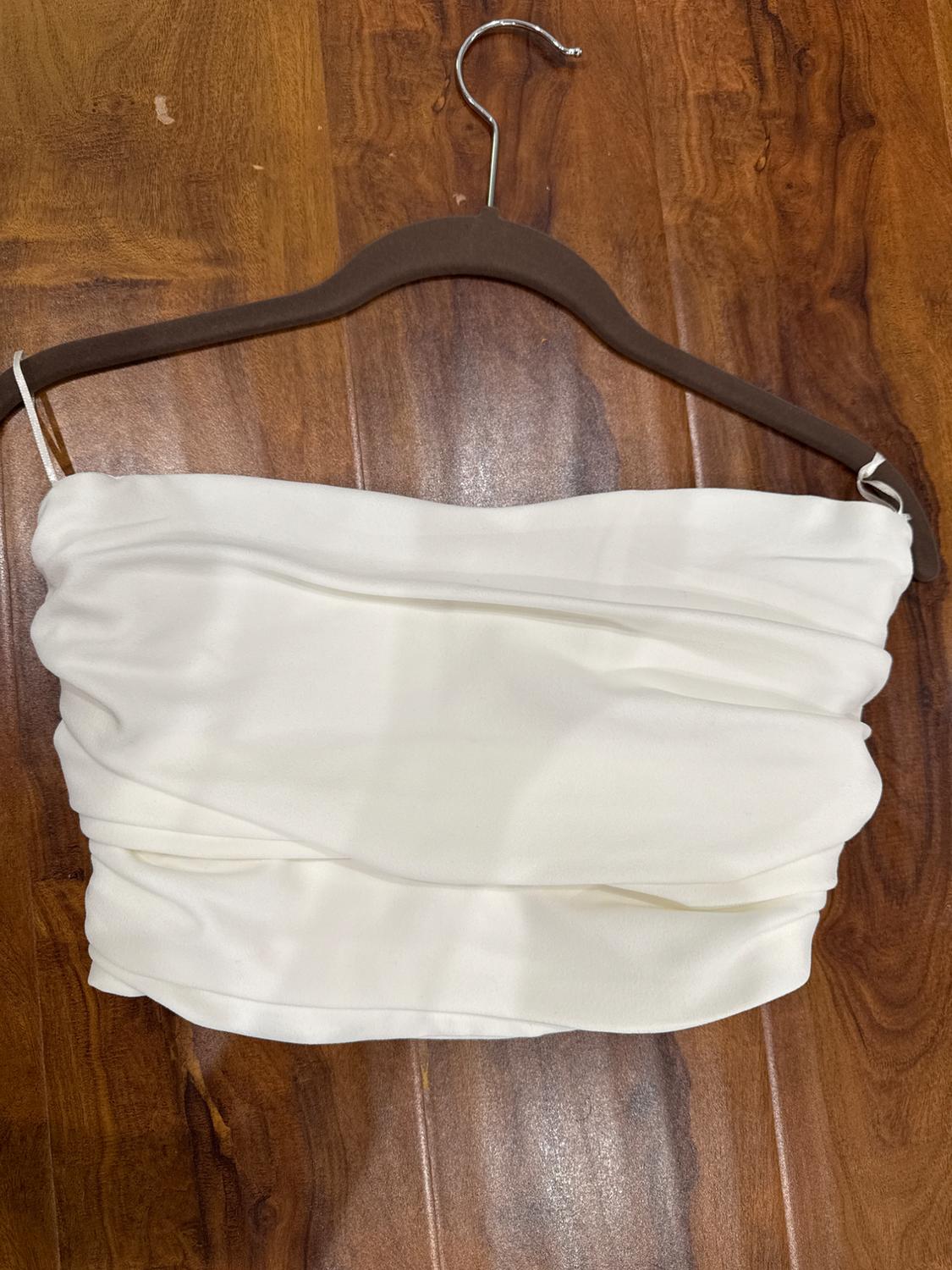 Draped white top hanging on a brown coat hanger over a wooden surface.