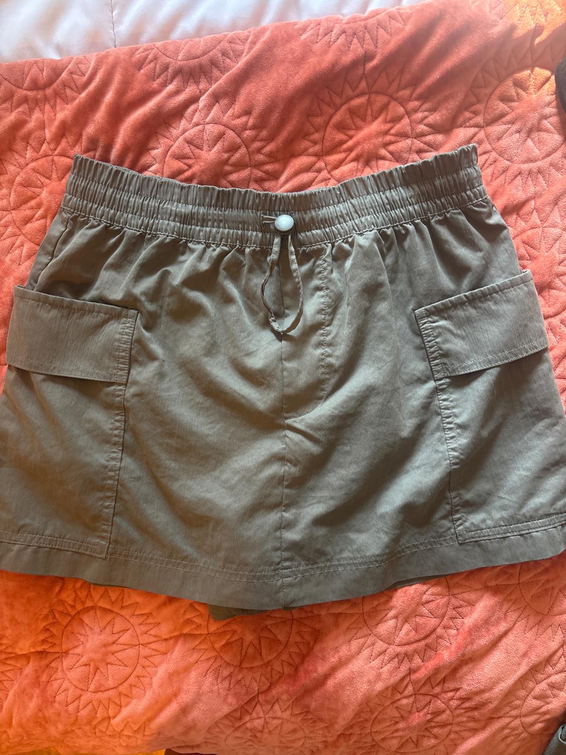 Khaki shorts with an elasticated waist, button and cargo pockets, on a textured orange blanket.
