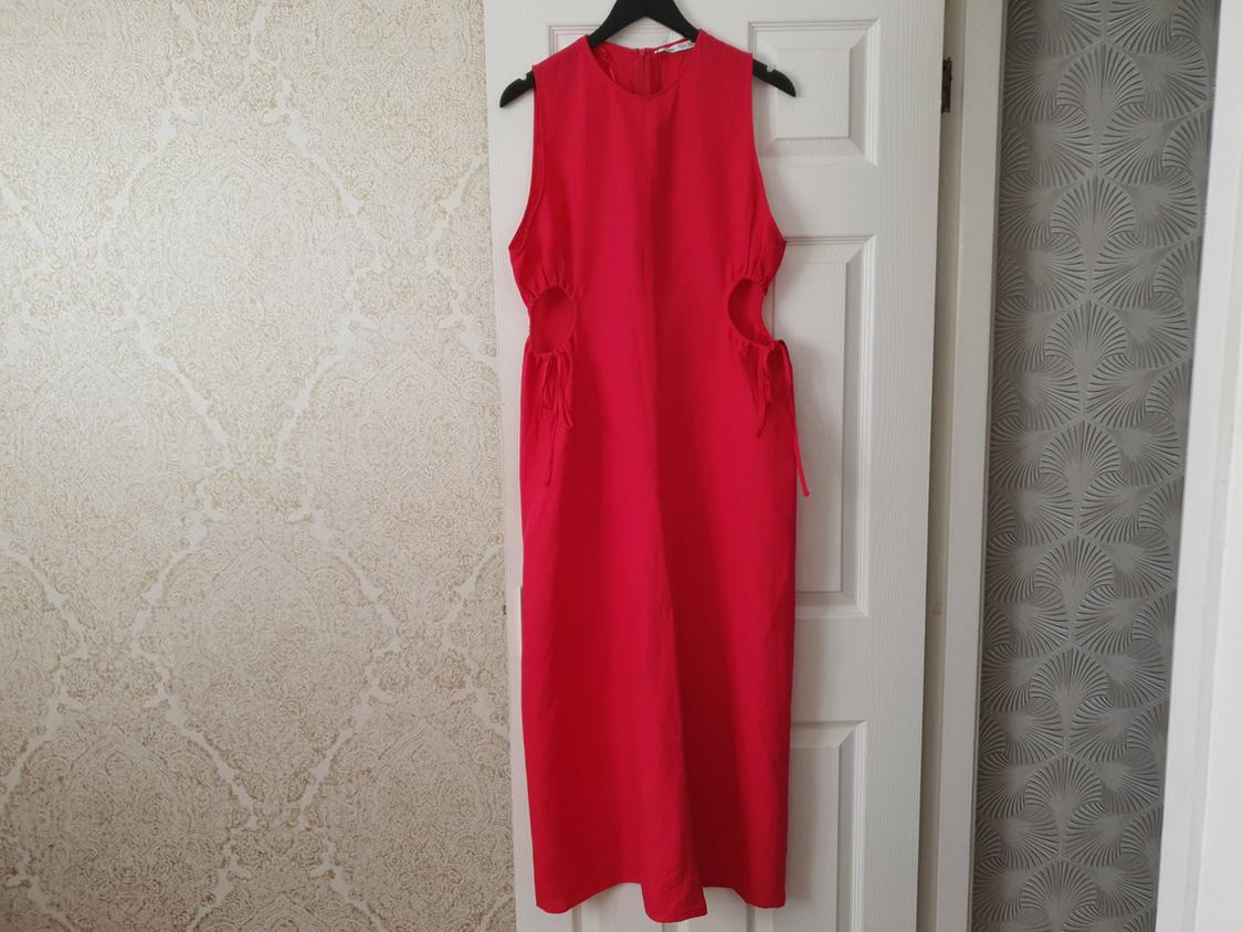 Red sleeveless dress with cut-outs and ties at the waist, hanging on a white door against a wallpaper background.