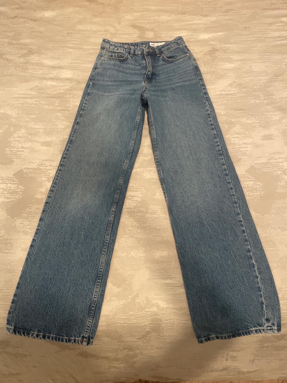 Light blue wide-leg jeans, placed on a textured beige surface.