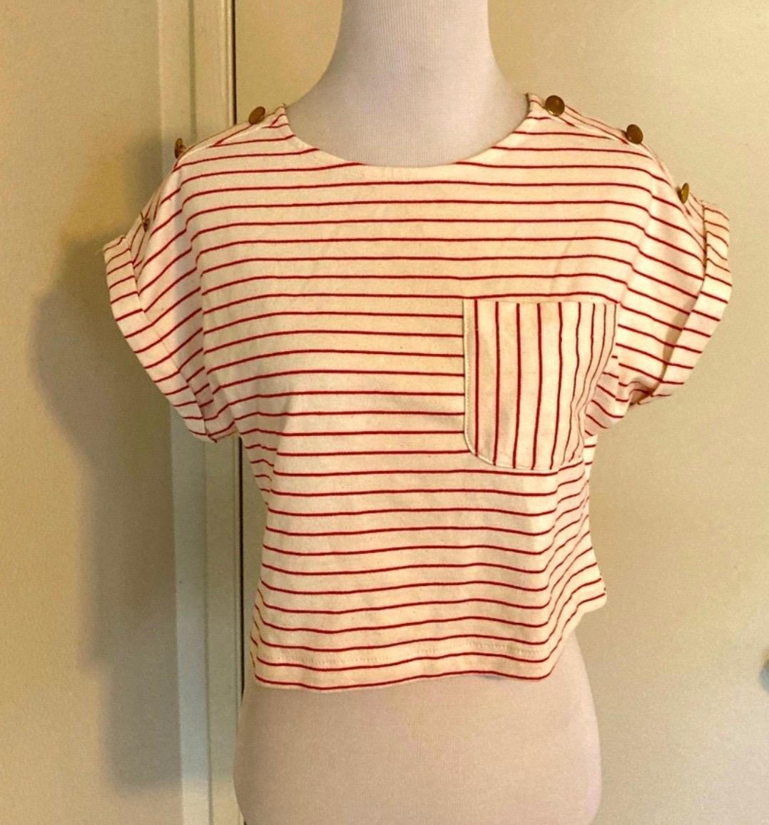 Mannequin in a red and white striped T-shirt, short sleeves with buttons on the shoulders and a chest pocket. Beige background.