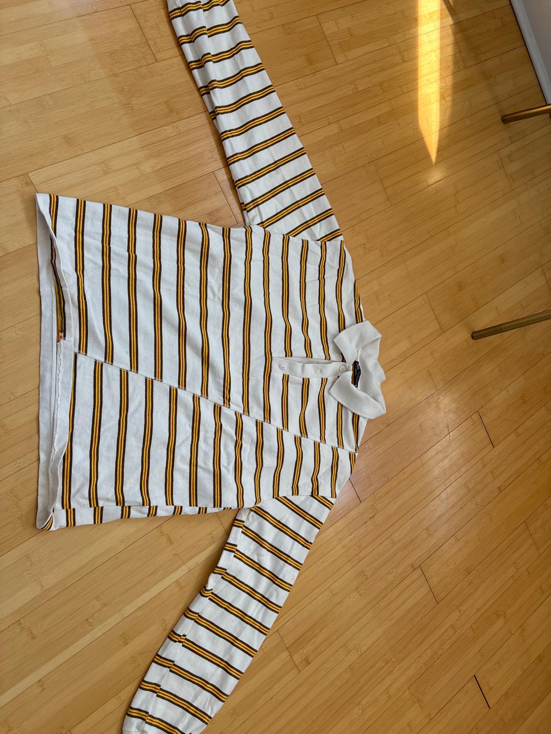 White, black, and mustard striped shirt spread out on a light wooden floor, with natural light illuminating the scene.
