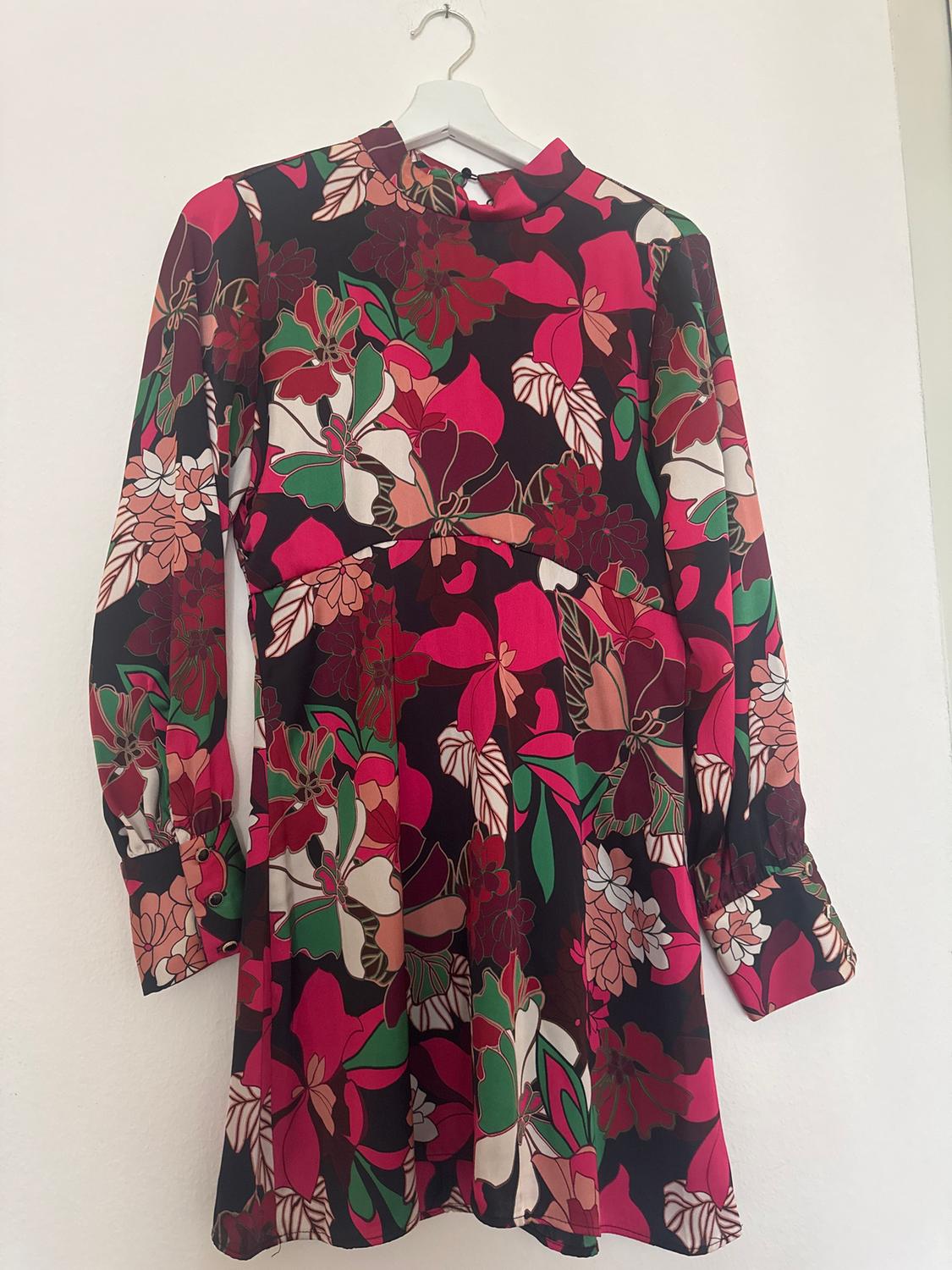 Long-sleeved dress with a floral print in red, green, and pink tones, hanging on a white hanger against a white background.