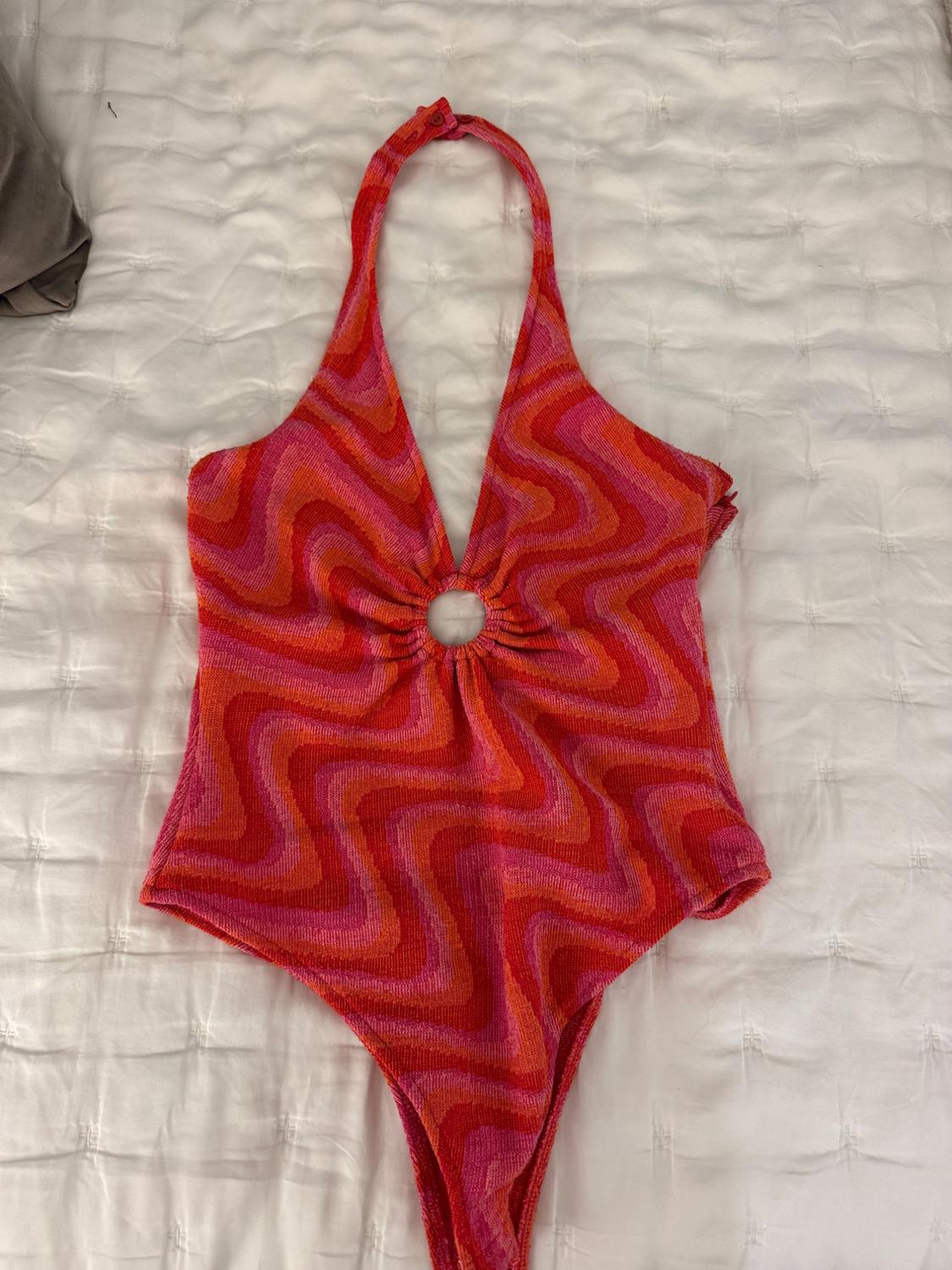 Red and pink bodysuit with psychedelic wave print, halterneck design with centre ring, on a white quilted bedspread.