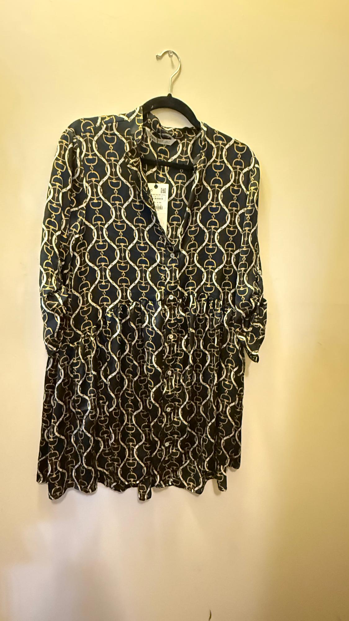 Dress hanging on a hanger with a gold chain print on a black background. Label visible on the collar. Beige background.