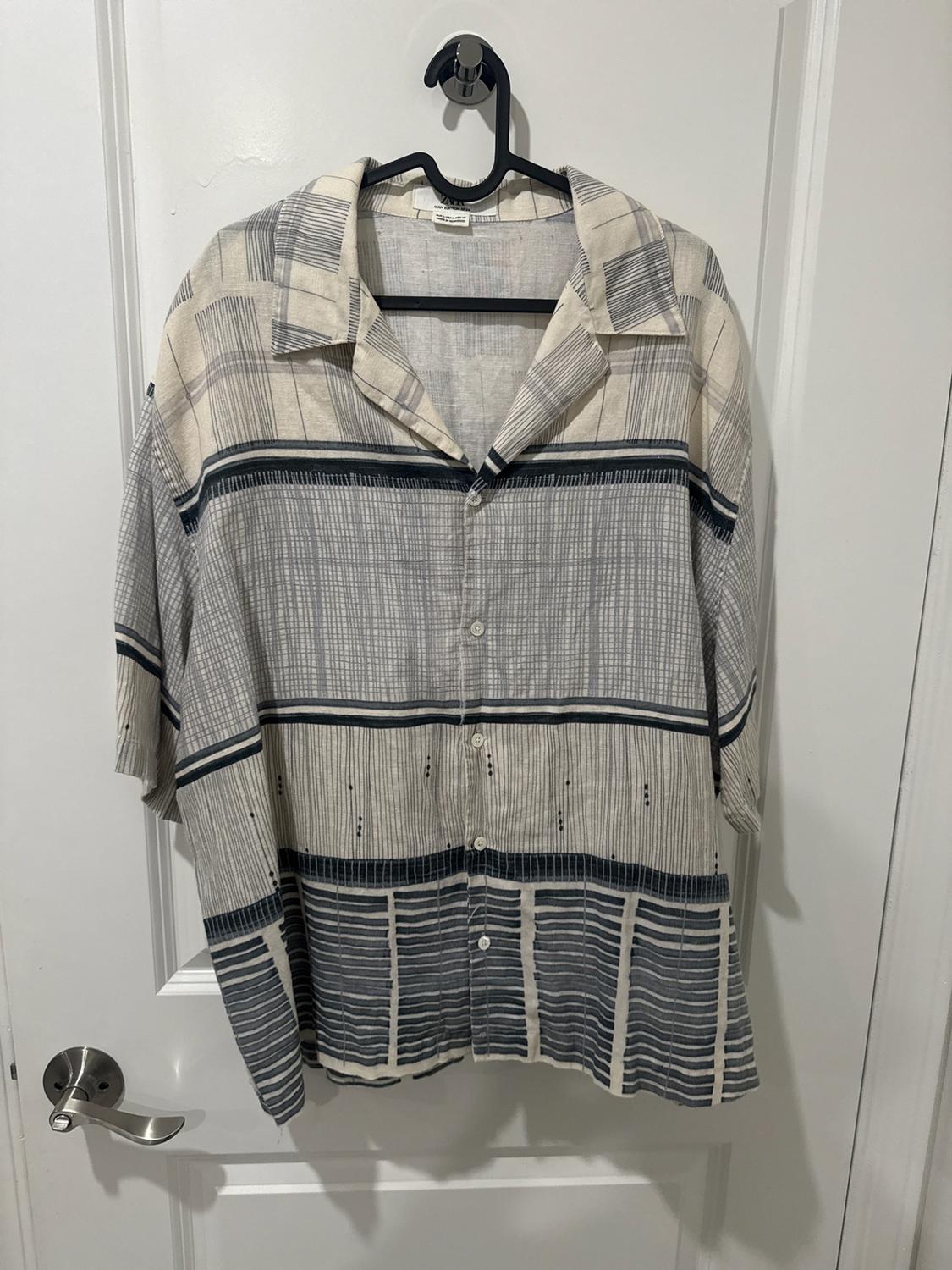 Short-sleeved shirt with a gray stripe and line pattern on a light background, hanging on a black hanger on a white door.