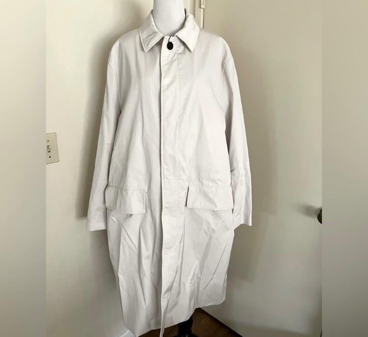 Long white coat on a mannequin, with a classic collar and front pockets, in a room with light-coloured walls.