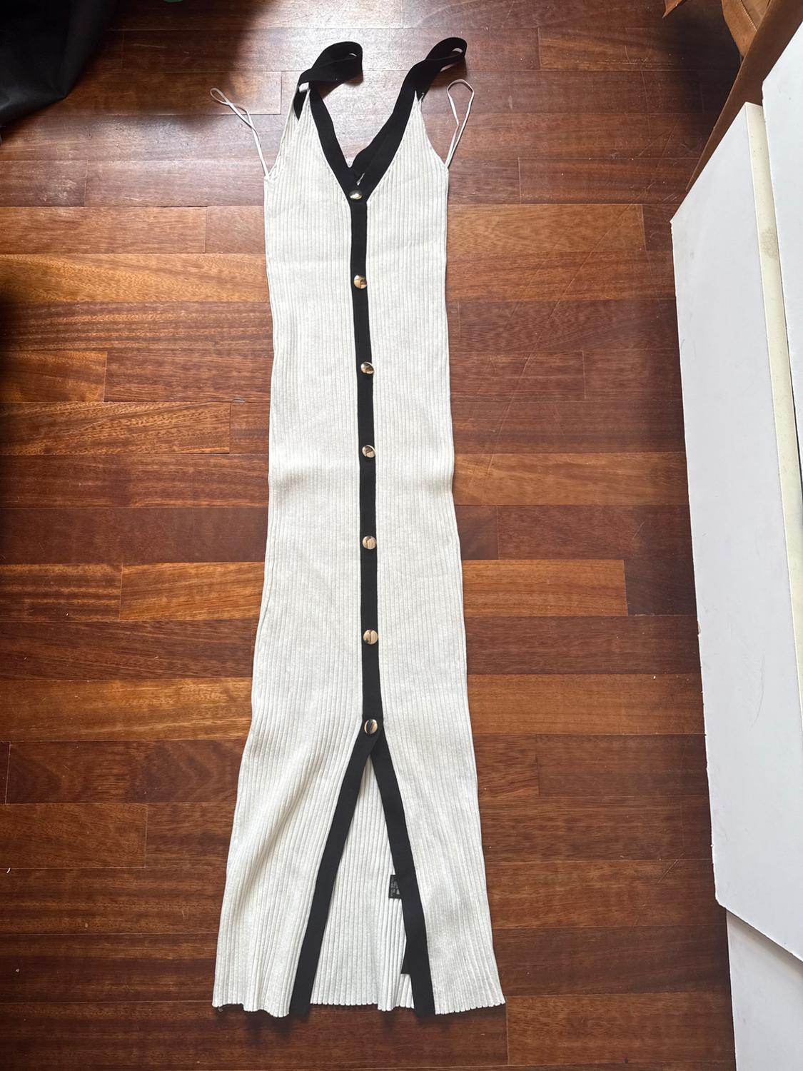 White ribbed knit maxi dress with gold buttons and black trim, on a wooden floor.
