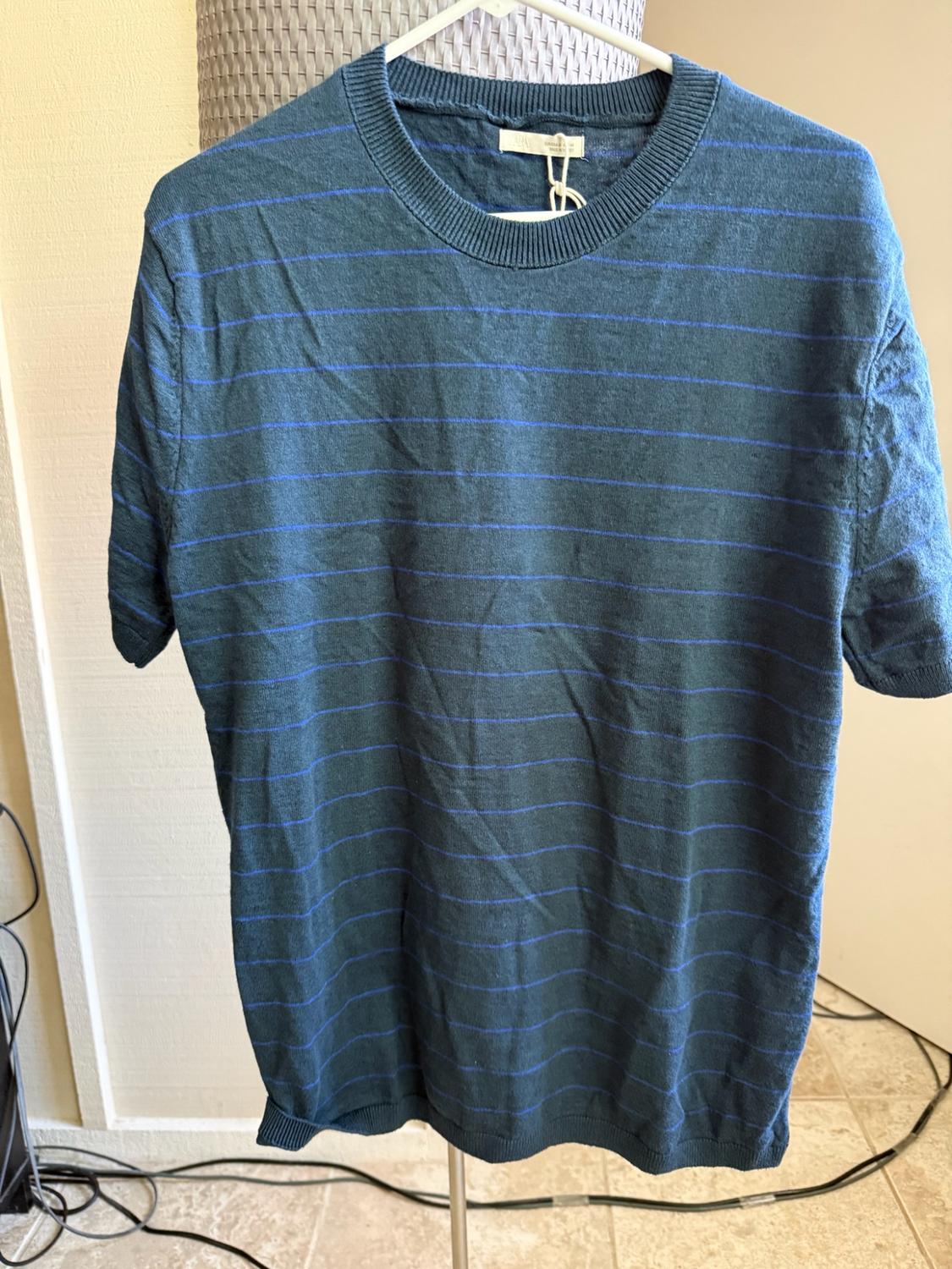 Navy-blue knitted T-shirt with fine horizontal stripes, hanging on a white hanger indoors.