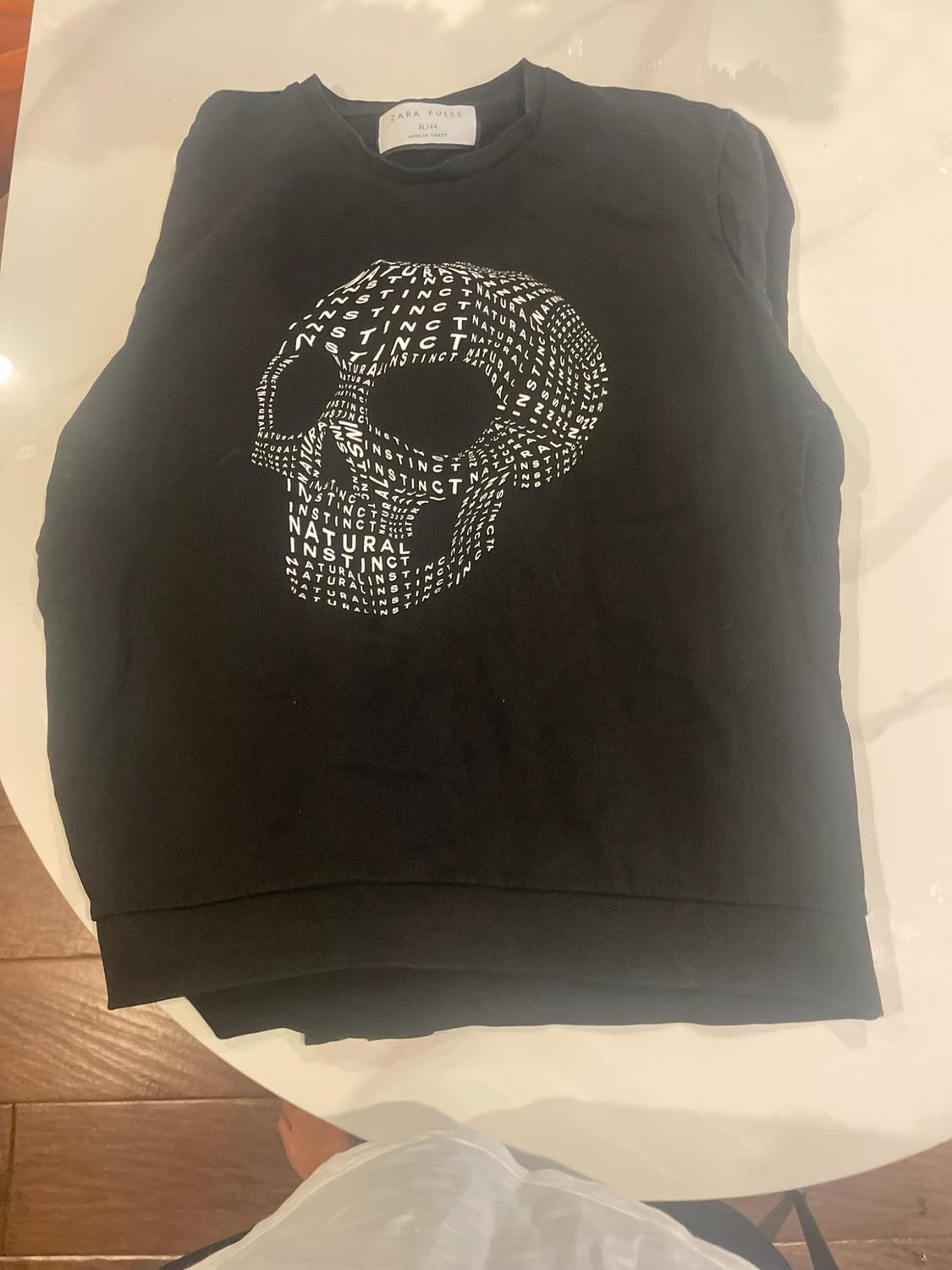 Black sweatshirt on a white table with a skull formed by the text "NATURAL INSTINCT". Tag "ZARA PULSE XL/44".