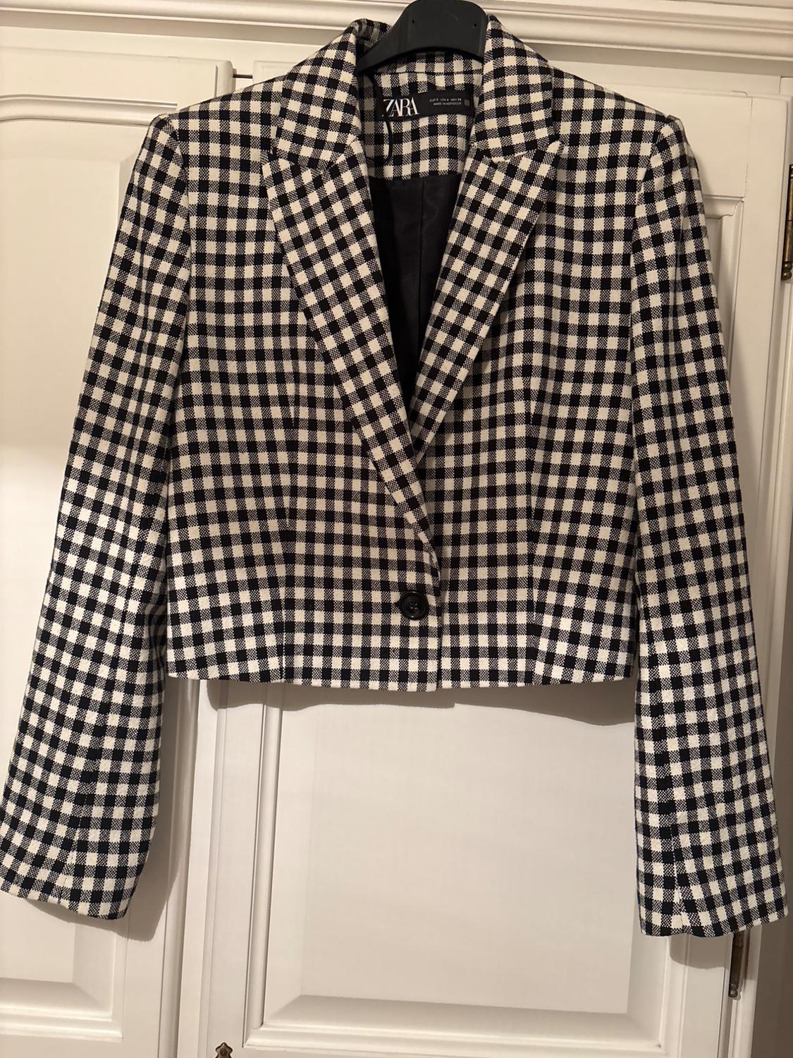 Black and white checked jacket hanging on a hanger. Visible brand label. White door background.
