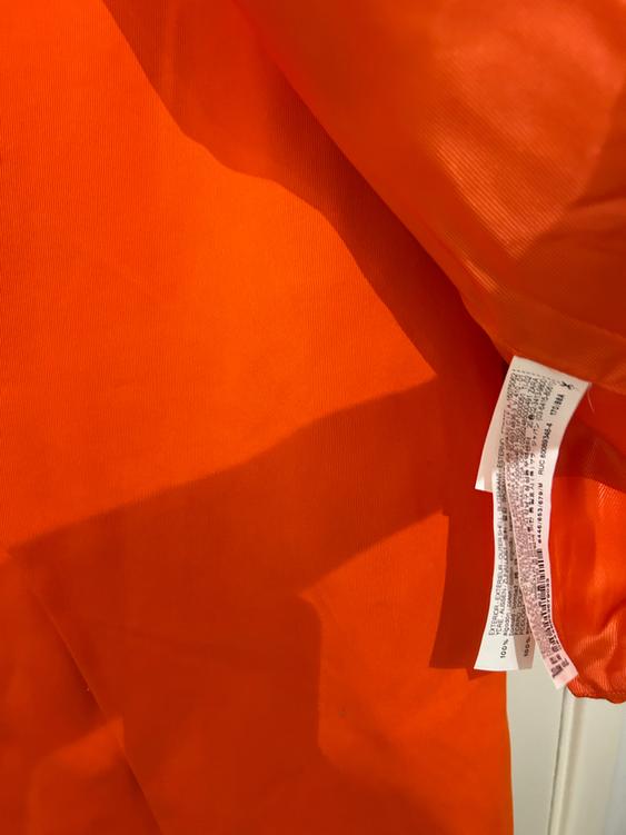 Bright orange fabric with white labels visible on the right edge, showing care instructions and material composition.