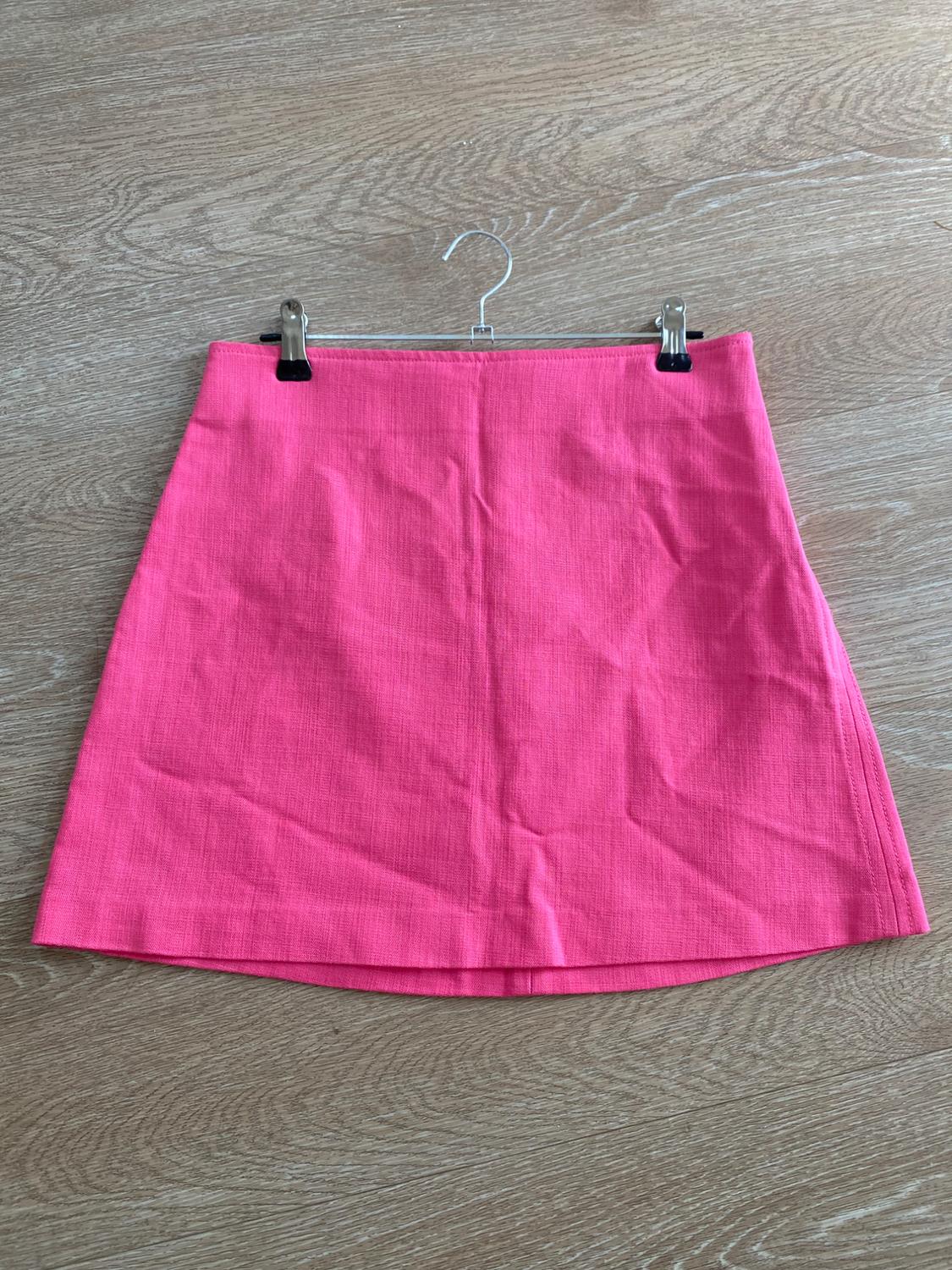 Pink short skirt hanging on a hanger against a light wooden background.