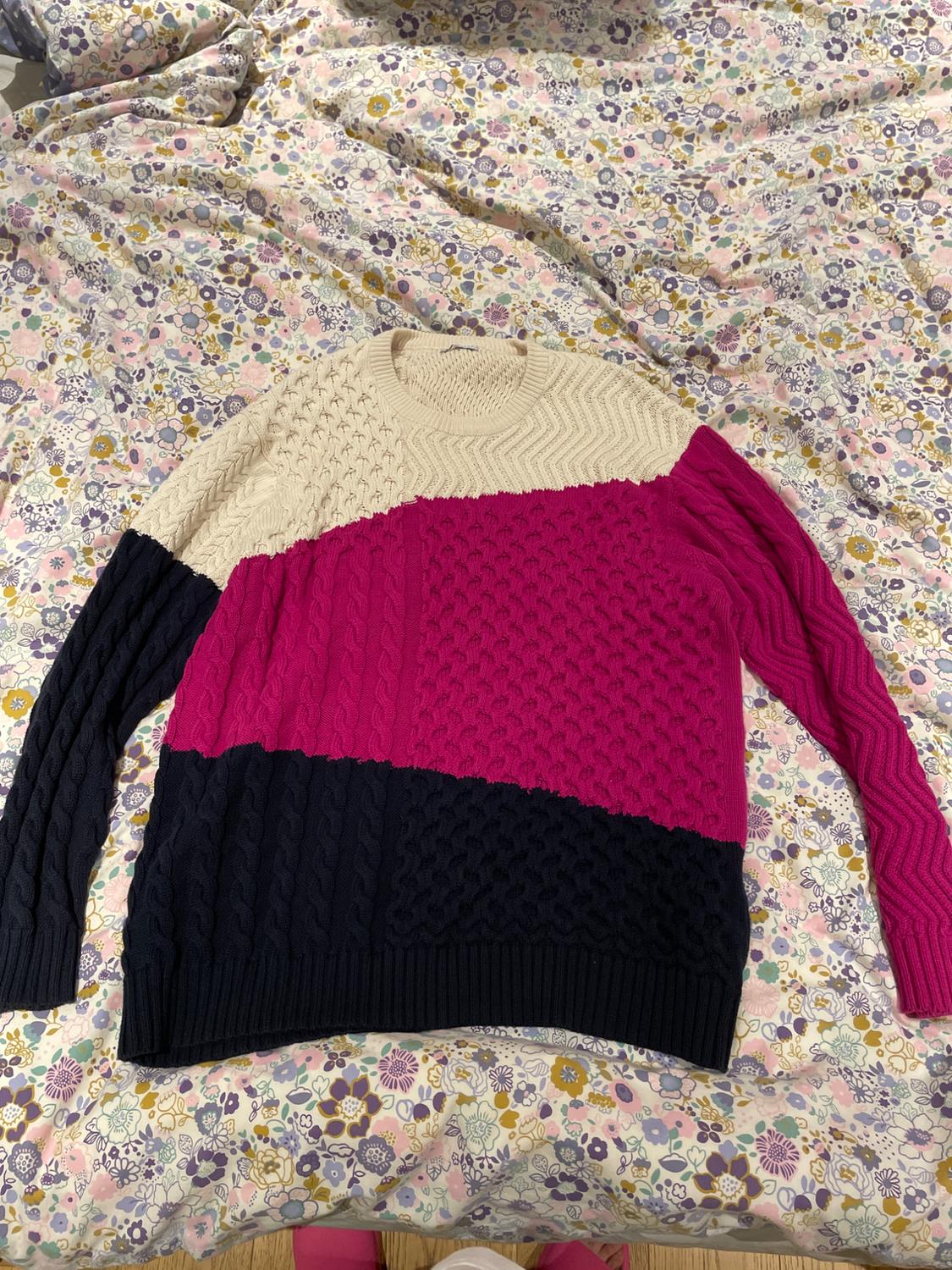 Tri-colour knitted jumper in cream, fuchsia, and black on a bed with a floral bedspread in pastel shades.