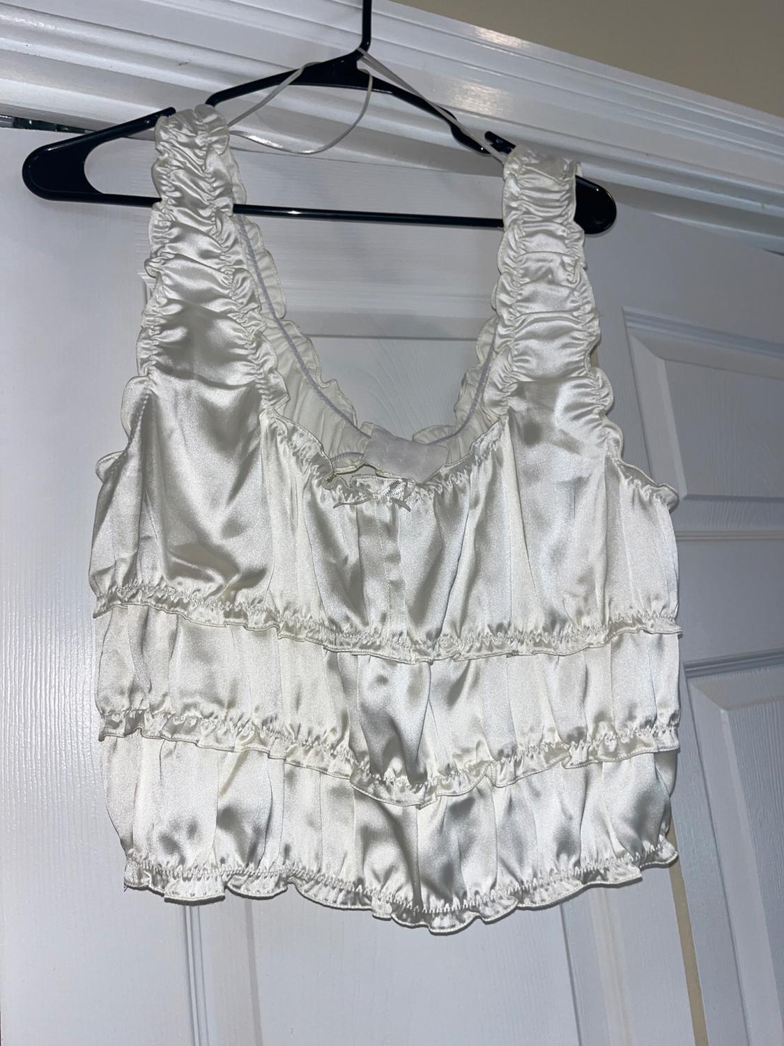 White ruffled satin top hanging on a black hanger over a white door.