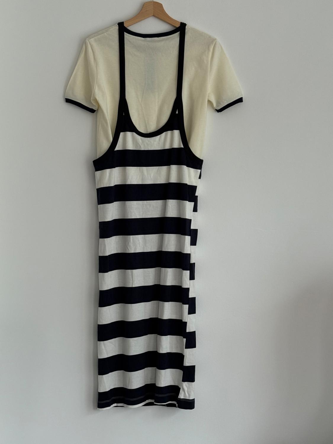 Stripey black and white sundress over a white t-shirt hanging on a wooden coat hanger against a white wall.
