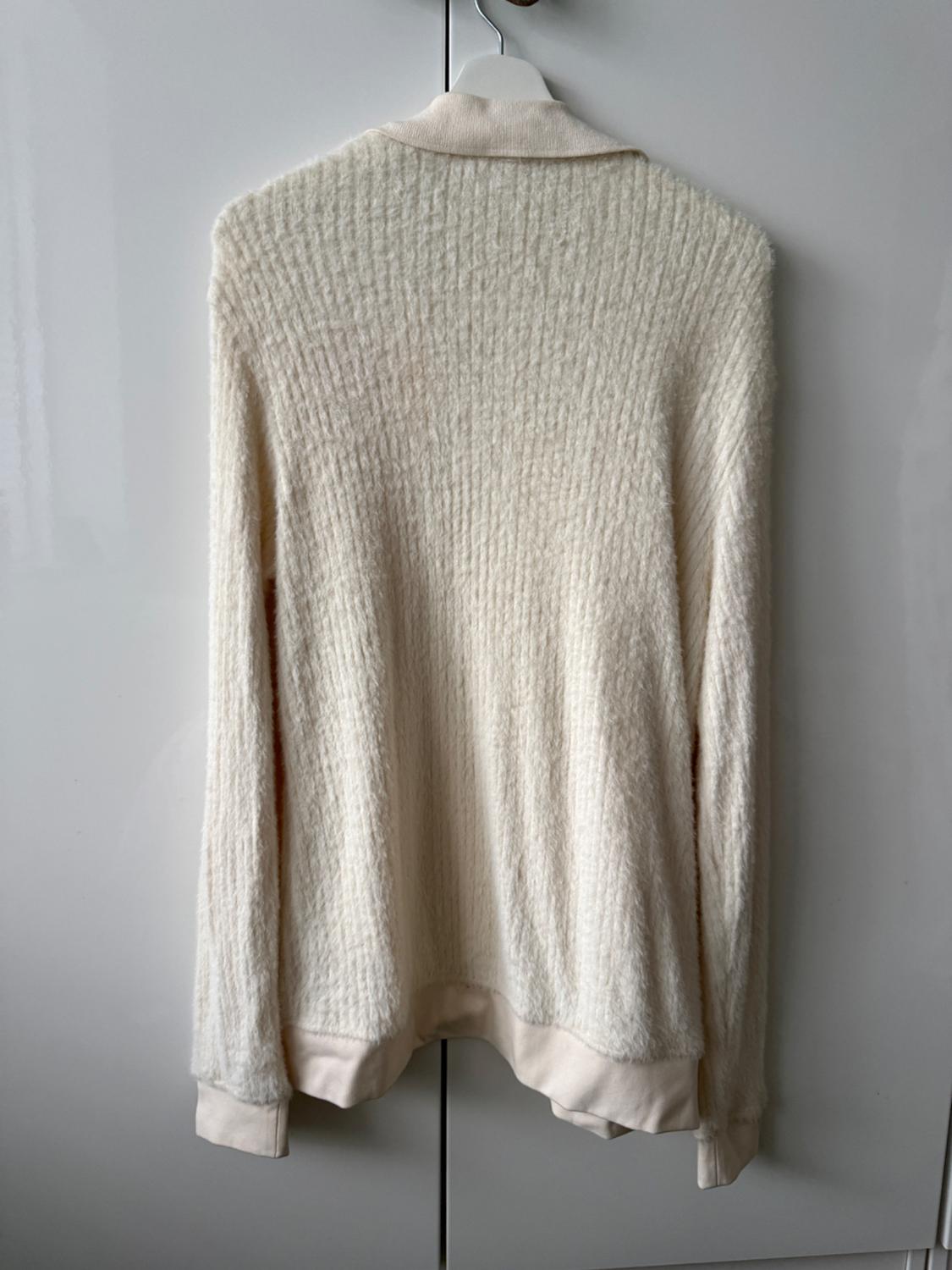White knitted jumper hanging on a white hanger in front of a light grey wardrobe.