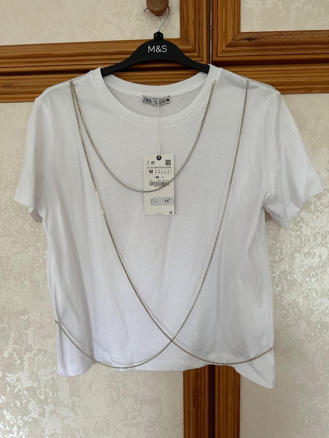 Front view of a white t-shirt with decorative chains and a swing tag.