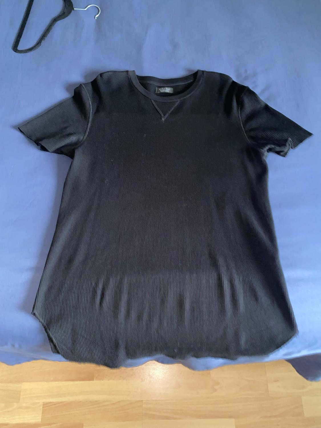 Black ribbed short-sleeve T-shirt on blue fabric. Part of a black hanger and a wooden floor can be seen at the bottom.