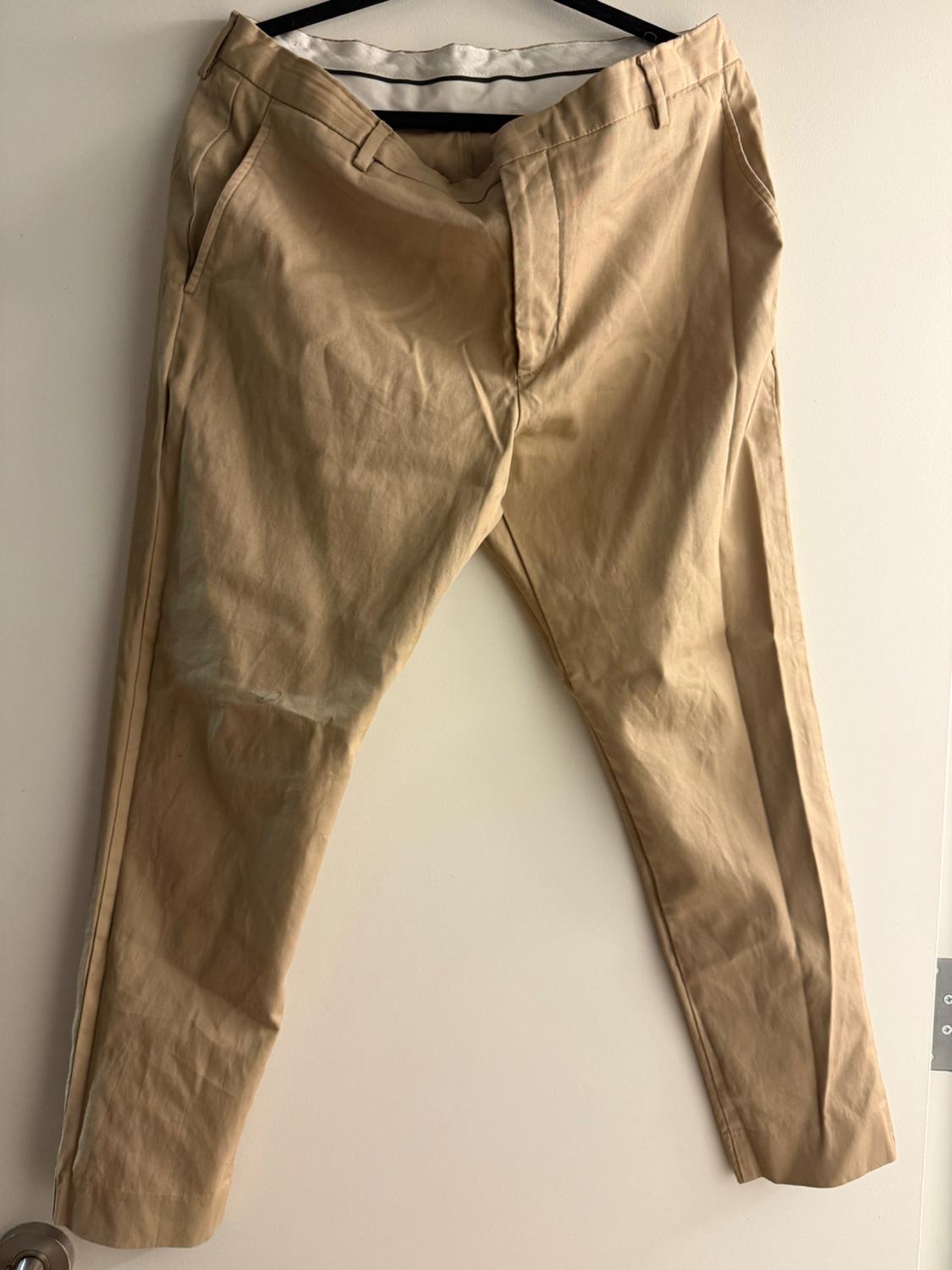 Beige trousers hanging on a black hanger over a white door. Wrinkled fabric and visible zip fastening.