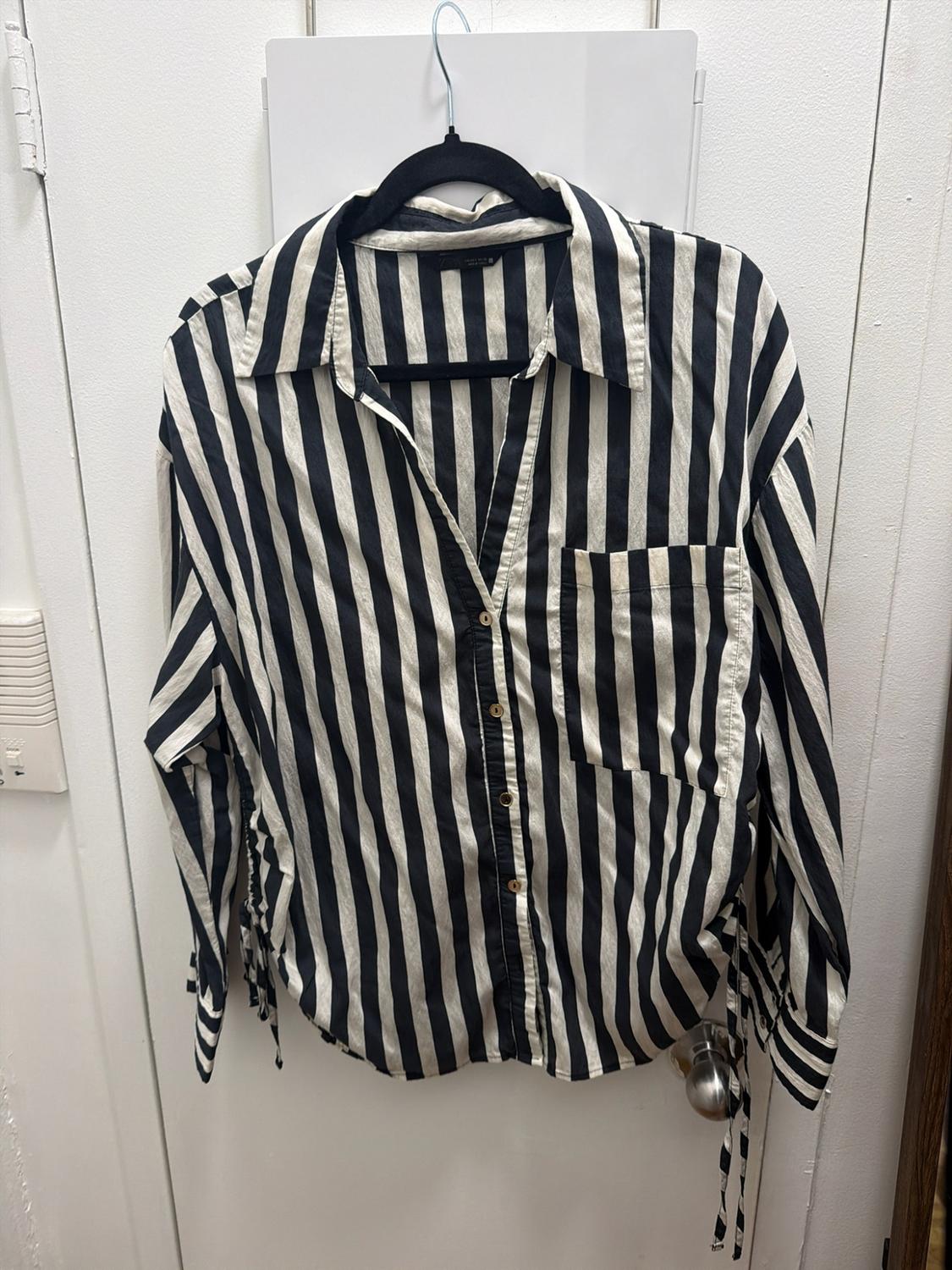 Black-and-white vertical striped shirt with buttons, a front pocket, and side ties, hanging on a white door.