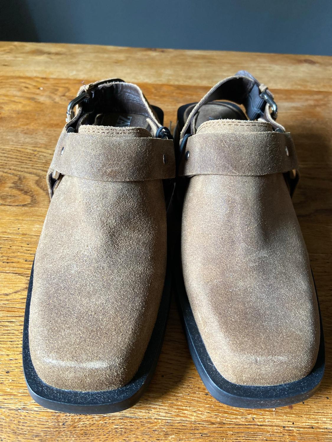 Brown suede shoes with a square toe, slingback strap, and black sole on wood. ZARA text on the inside.