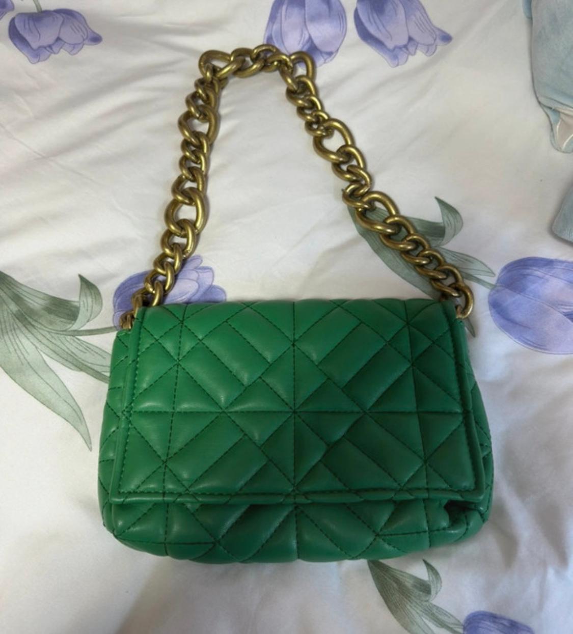 Quilted green handbag with a gold chain on white fabric with a purple floral and green leaf print.