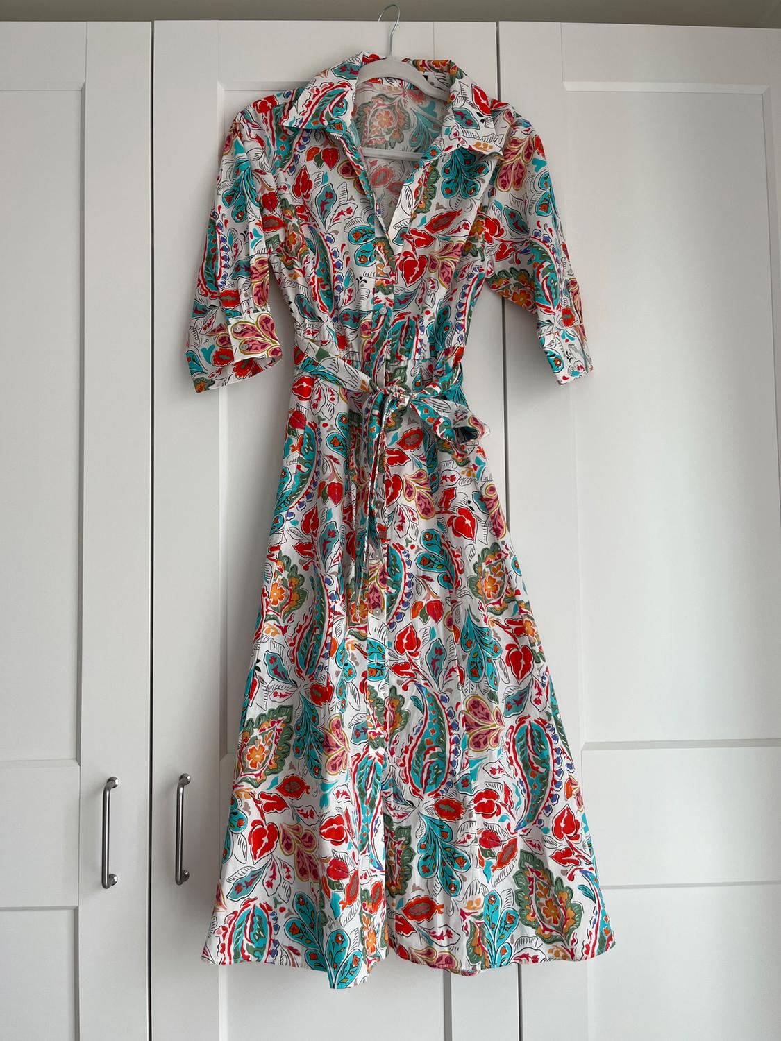 Dress hanging on a white door, with a colourful floral pattern in shades of red, green, and blue, and a matching belt.