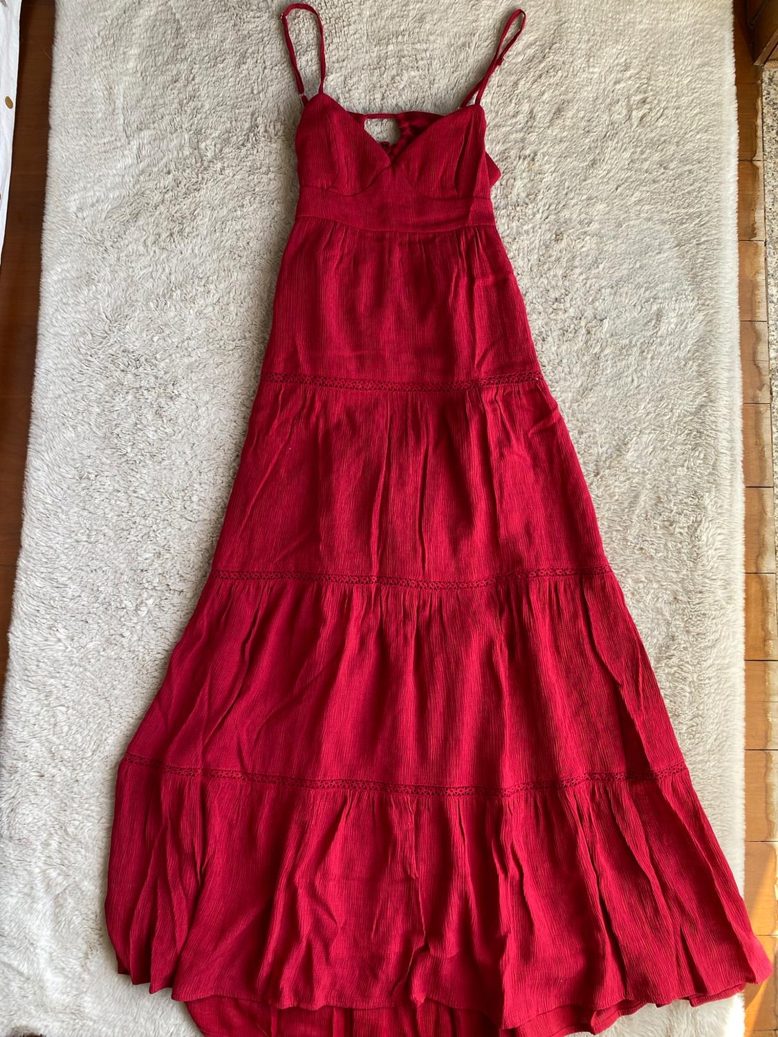 Long red dress with thin straps and a tiered skirt, photographed on a white shaggy rug on a wooden floor.