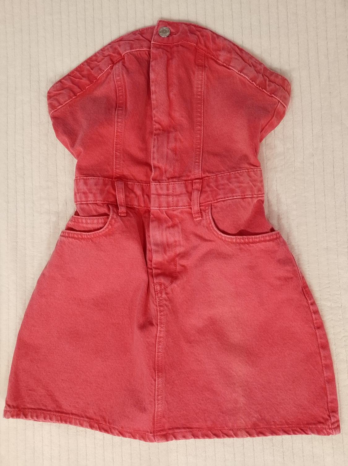 Red strapless denim mini dress with front buttons and pockets, laid flat on a light textured fabric background.