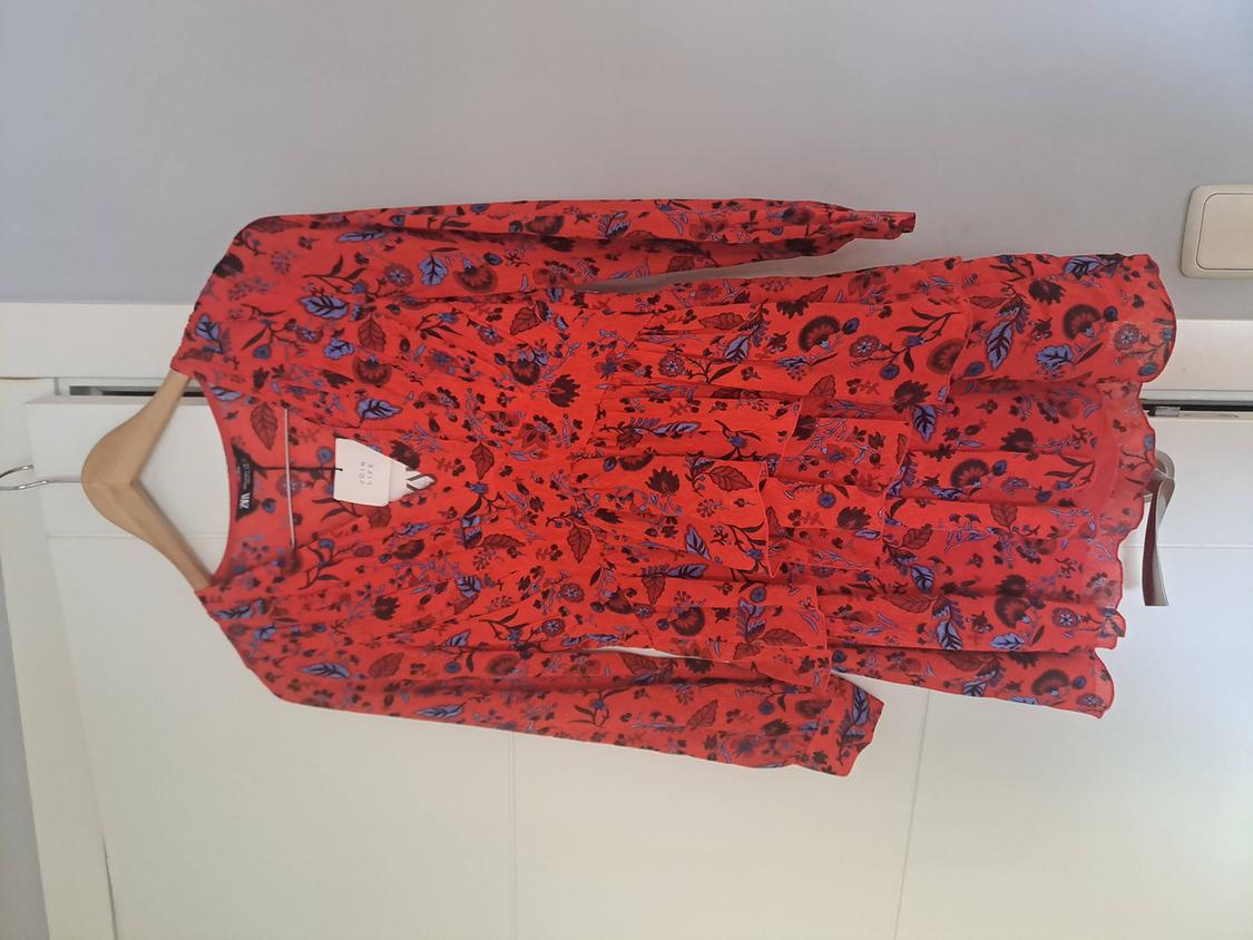 Red long-sleeved floral-print dress hanging on a wooden hanger against a white door. Labels reading ZARA and JOIN LIFE.