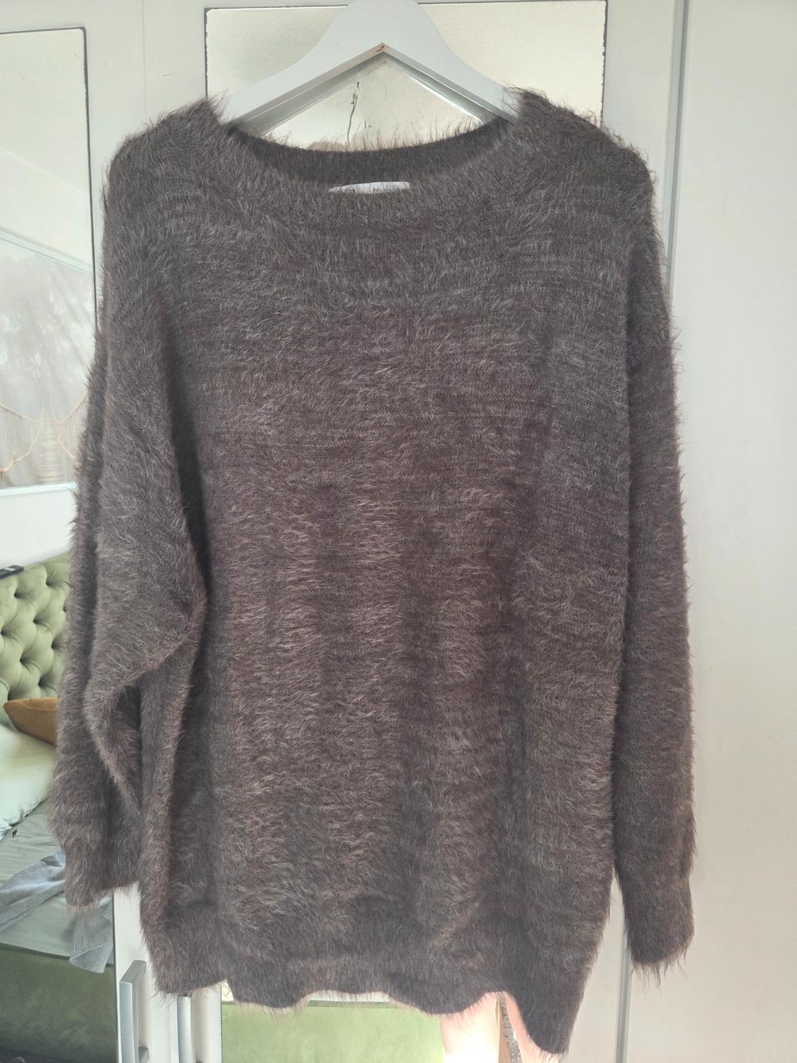Brown jumper with a faux-fur effect hanging on a white coat hanger in front of a mirror reflecting a room with a green bed.