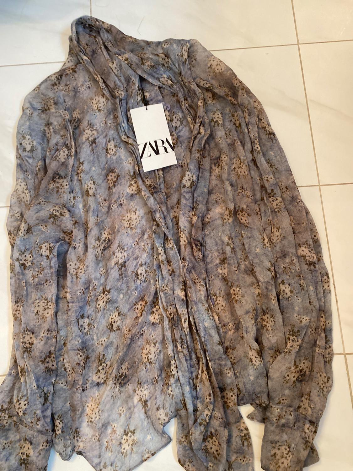 Front view of a floral print blouse in blue and beige tones with a visible tag.