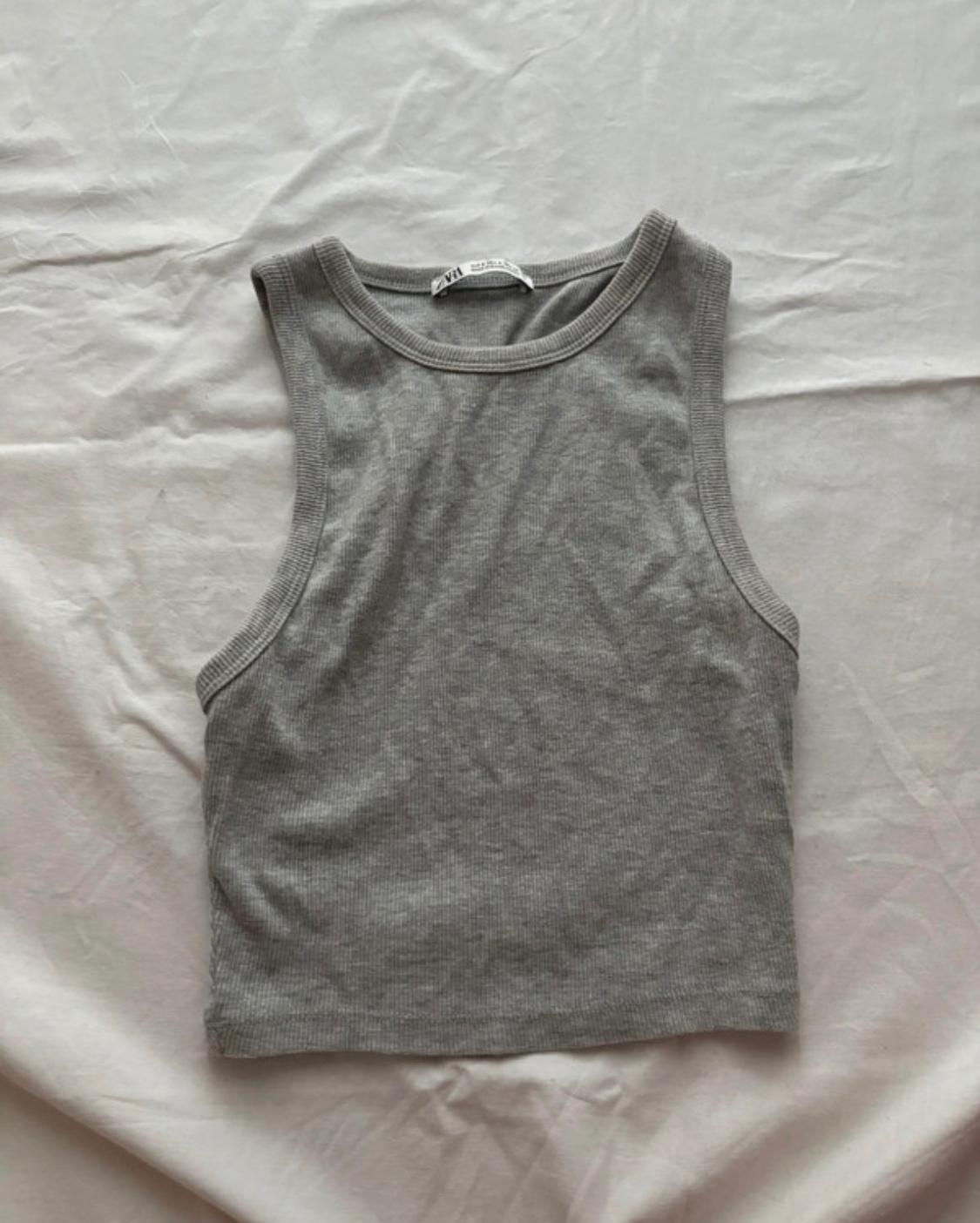 Grey cropped sleeveless round-neck top in ribbed fabric, on a crumpled white sheet.