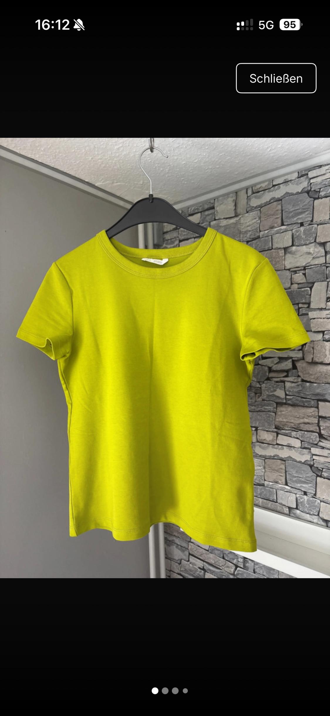 Lime green short-sleeved T-shirt on a black hanger. Grey and stone wall background. Text: 16:12 5G 95 Close.