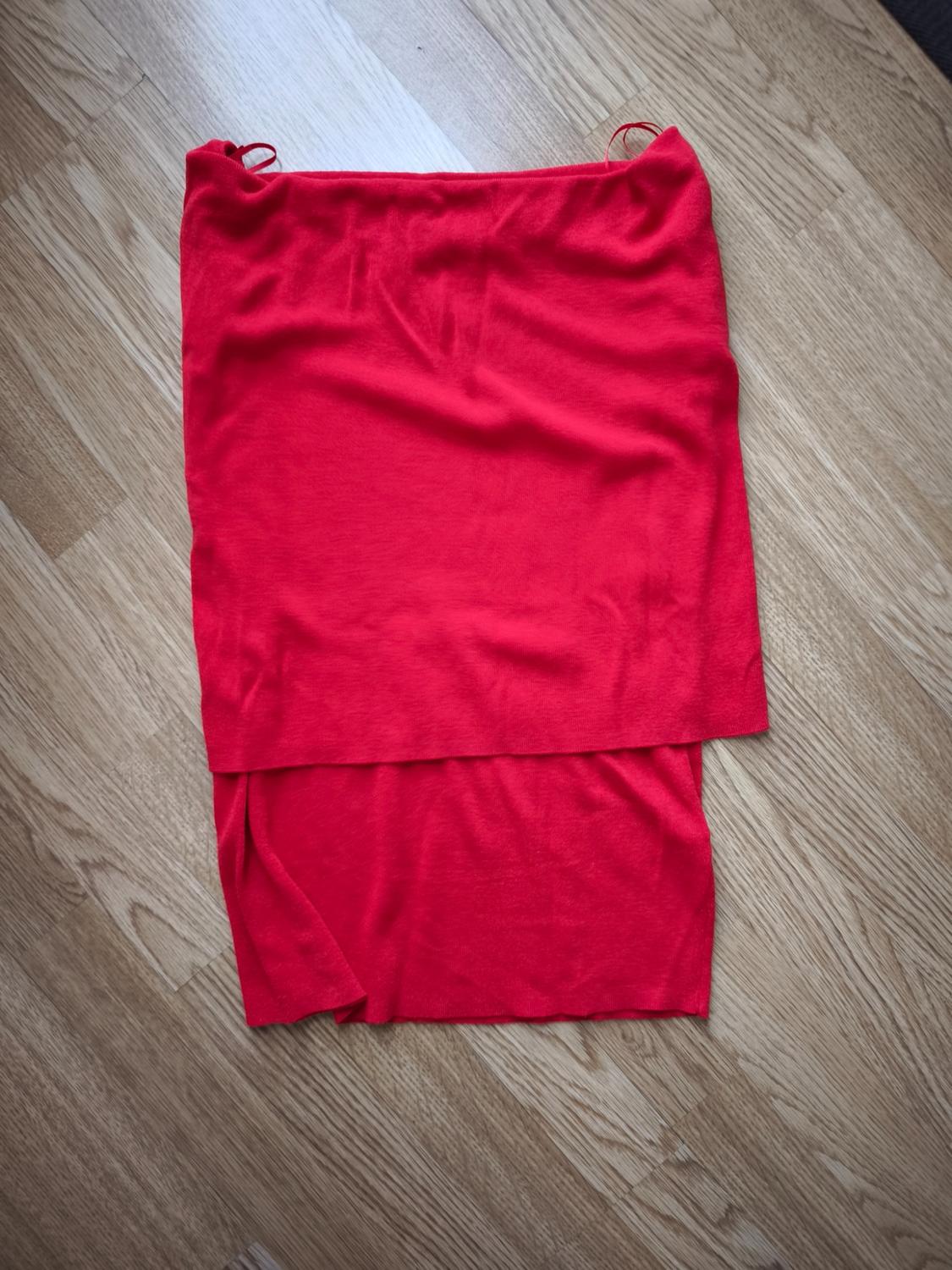 Light red fabric skirt spread out on a light wooden floor, showing a simple and elegant design.