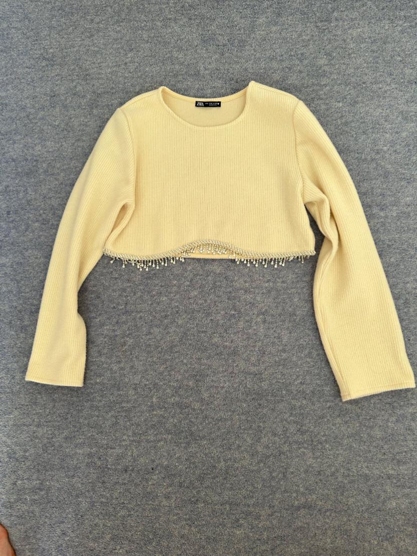 Front view of a short beige jumper with long sleeves and pearl trim on the hem.