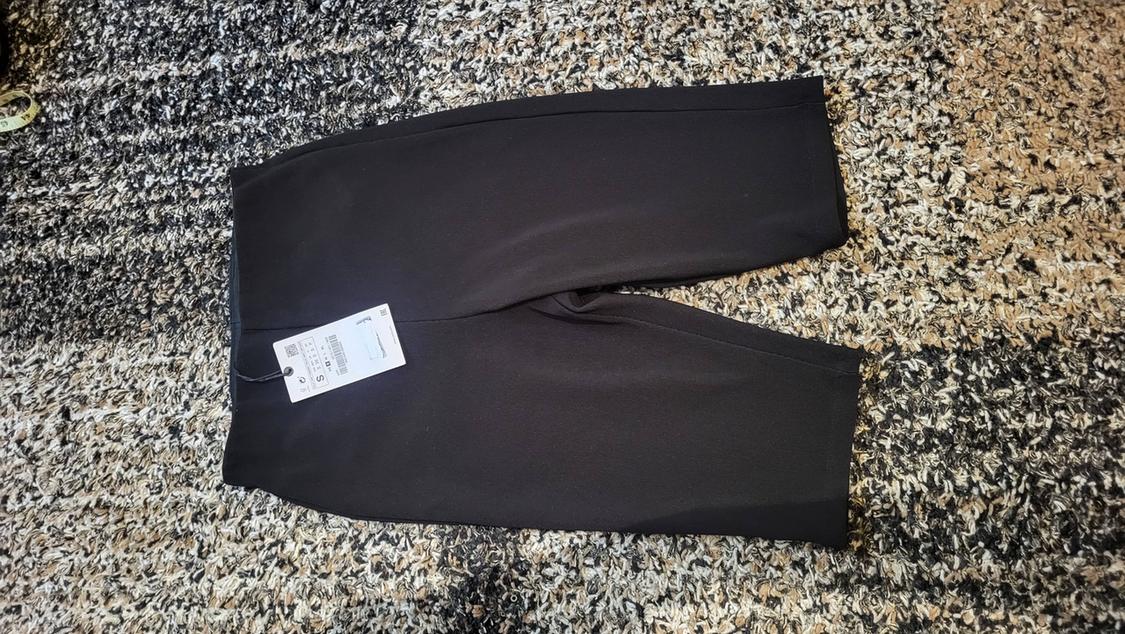 Black shorts on a textured grey and beige rug. White tag with size and price details attached.