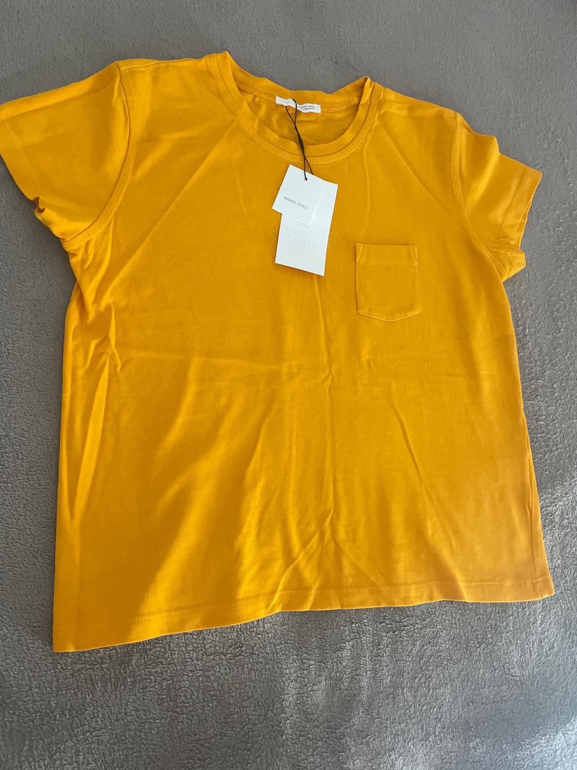 Yellow short-sleeved t-shirt with a pocket on a grey surface. Label with the text "WASHED EFFECT ZARA".