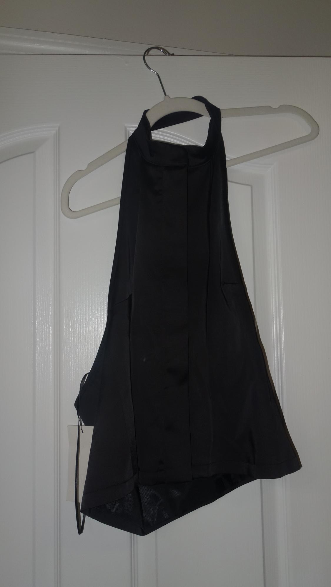 Black sleeveless top hanging on a white hanger over a white door. Smooth fabric and elegant design.