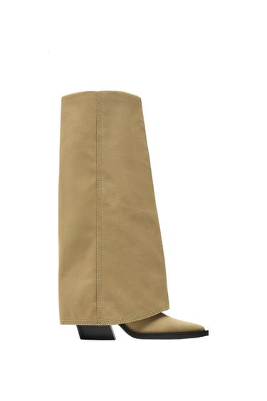 Side view of a beige high boot with a black square heel.