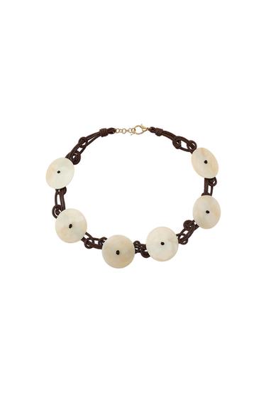 Knotted brown cord necklace with cream-coloured round discs. Gold-tone clasp on a white background.