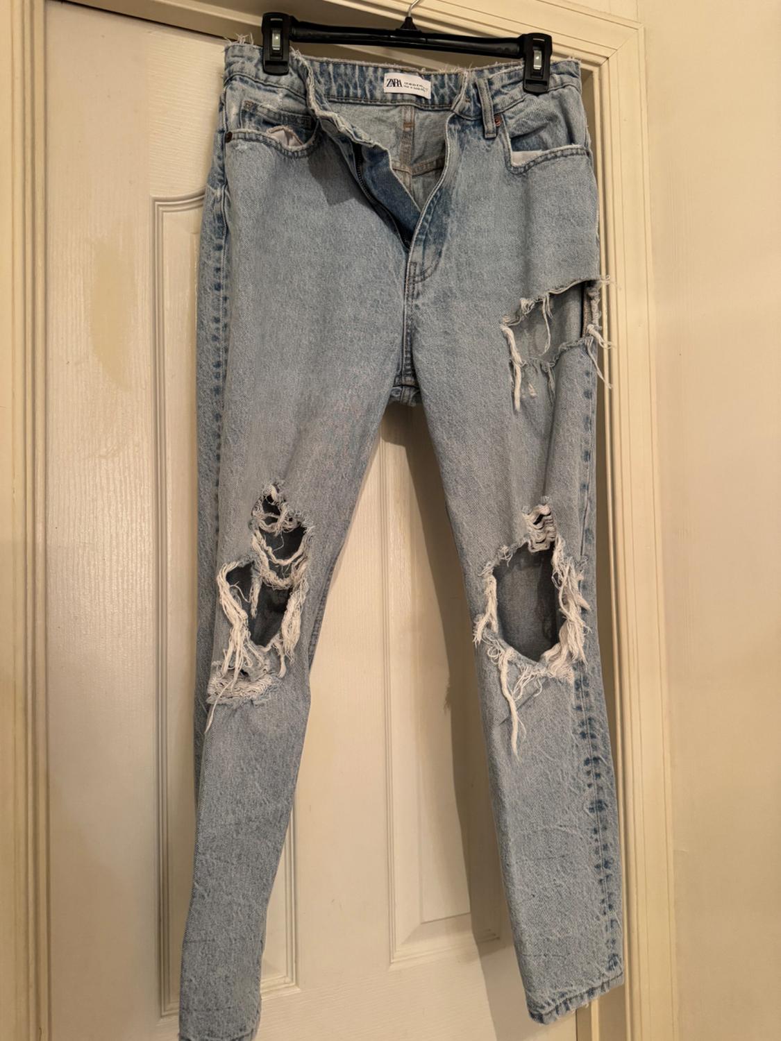 Front view of distressed blue jeans with rips on the legs and visible side pockets.