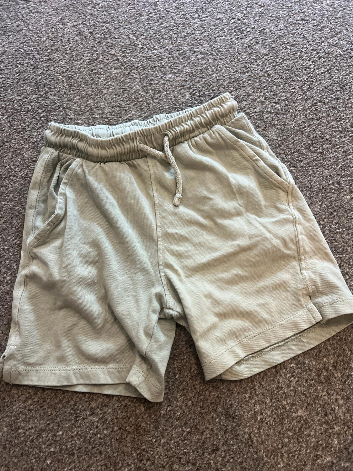 Light green casual shorts with an elasticated waistband, drawstring and side pockets, on a grey carpet.