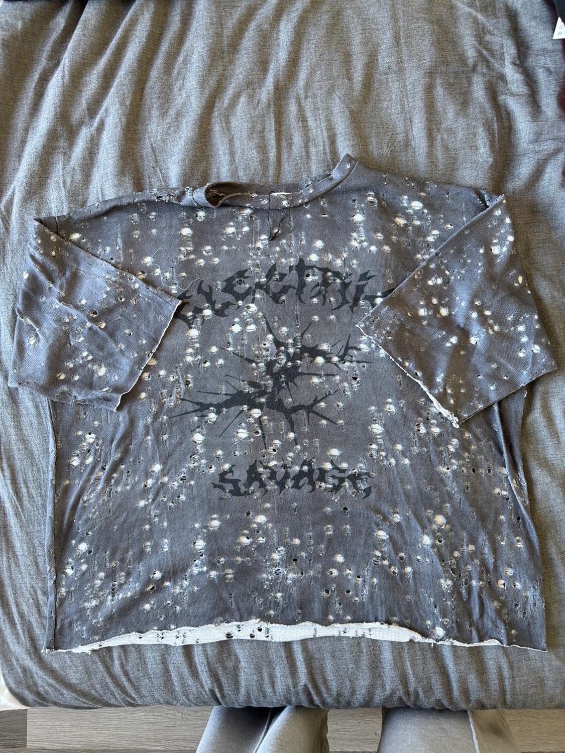 Grey t-shirt with white splatter design and illegible black text in the centre, on a grey fabric surface.
