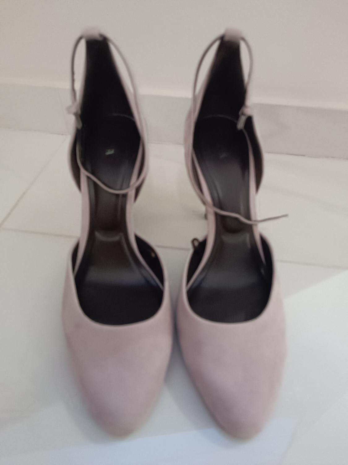 Pale pink high-heeled shoes with ankle straps, placed on a white floor.
