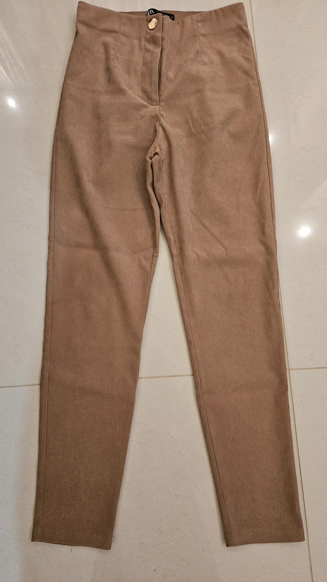 High-waisted brown trousers with a light button, placed on a light floor.