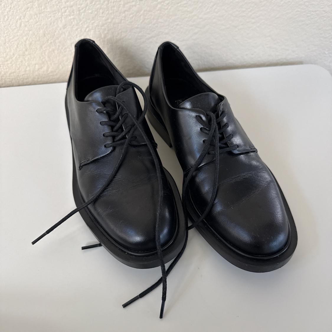 Black leather lace-up shoes on a white surface, showcasing a classic and elegant design.