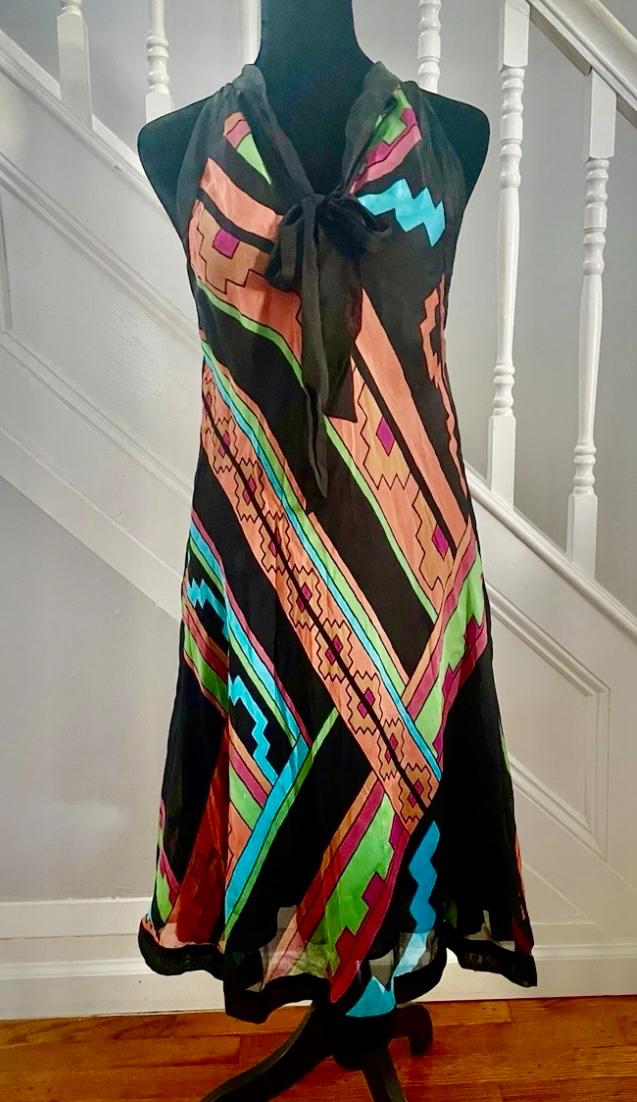 Sleeveless dress with geometric print in black, pink, green, and blue, displayed on a mannequin in front of a white staircase.